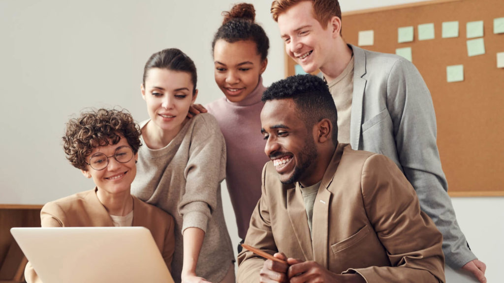 Agence de marketing digital Équipe souriante rassemblée autour d’un ordinateur, illustrant le gain de temps et la collaboration.